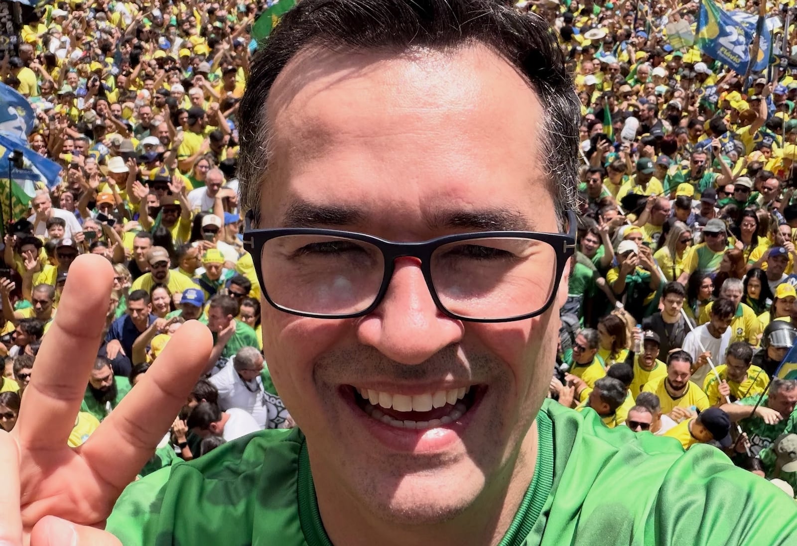 Homem de camiseta verde faz gesto com a mão em manifestação