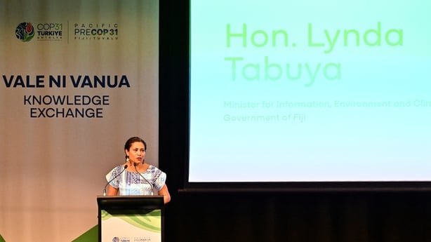 Lynda Tabuya speaking at pre-COP summit, her title is displayed on a large screen behind her.